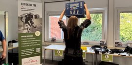 Exoskelett im Einsatz: Über-Kopf-Arbeit Eine Frau hebt eine Getränkekiste über den Kopf