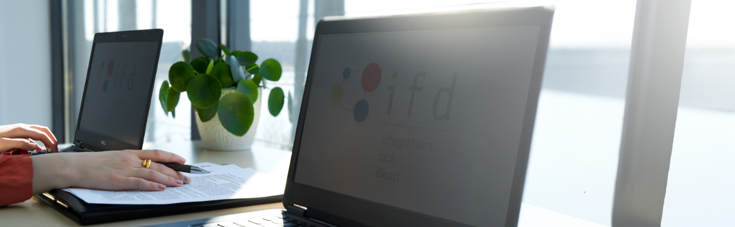 Zwei Laptops mit einer Person, die auf einem der Laptops tippt Zwei Laptops stehen auf einem Tisch und jemand tippt auf dem linken Laptop. Eine Akte liegt daneben.