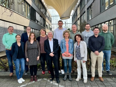 Gruppenbild von 13 Personen zwischen zwei Gebäuden