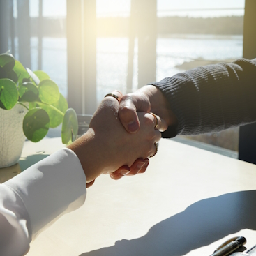Zwei Personen, die sich über einem Tisch die Hand geben.