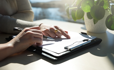 Person schreibt Notizen auf einem Klemmbrett Eine Person, die mit einem Stift auf einem Klemmbrett schreibt.