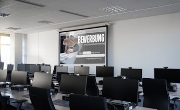 Computerraum mit Präsentation zum Thema Bewerbung Man sieht einen Raum mit vielen Computern und die Projektion einer Präsentation vorne im Raum.