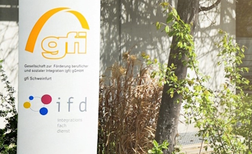 Außenbereich mit einem Aufsteller, auf dem die Logos der gfi und des ifd zu sehen sind.