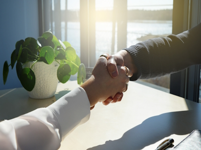 Zwei Personen, die sich die Hand geben Zwei Personen, die sich über einem Tisch die Hand geben.