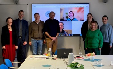 Sieben Personen stehen vor einer Leinwand mit 2 weiteren Personen.